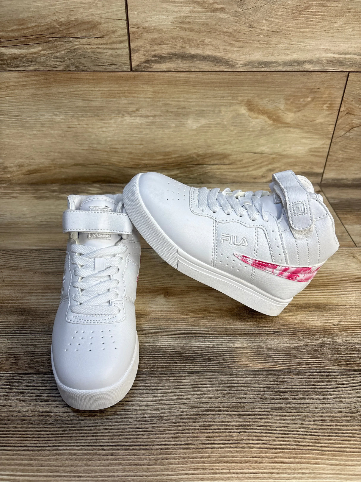White kids Fila high-top sneakers with pink accent, on wood background