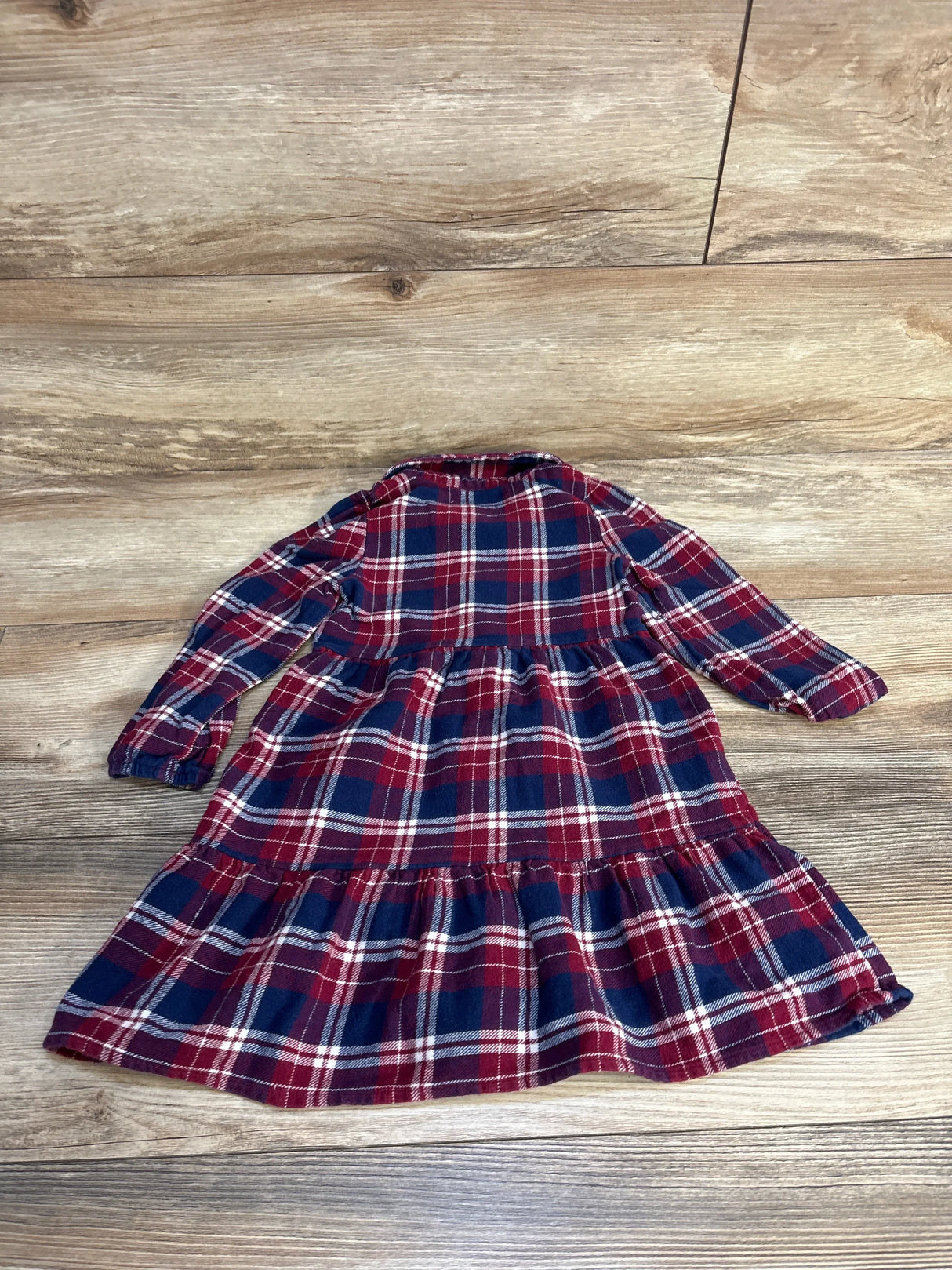 Long sleeve red and navy plaid toddler dress with ruffle skirt on wood background