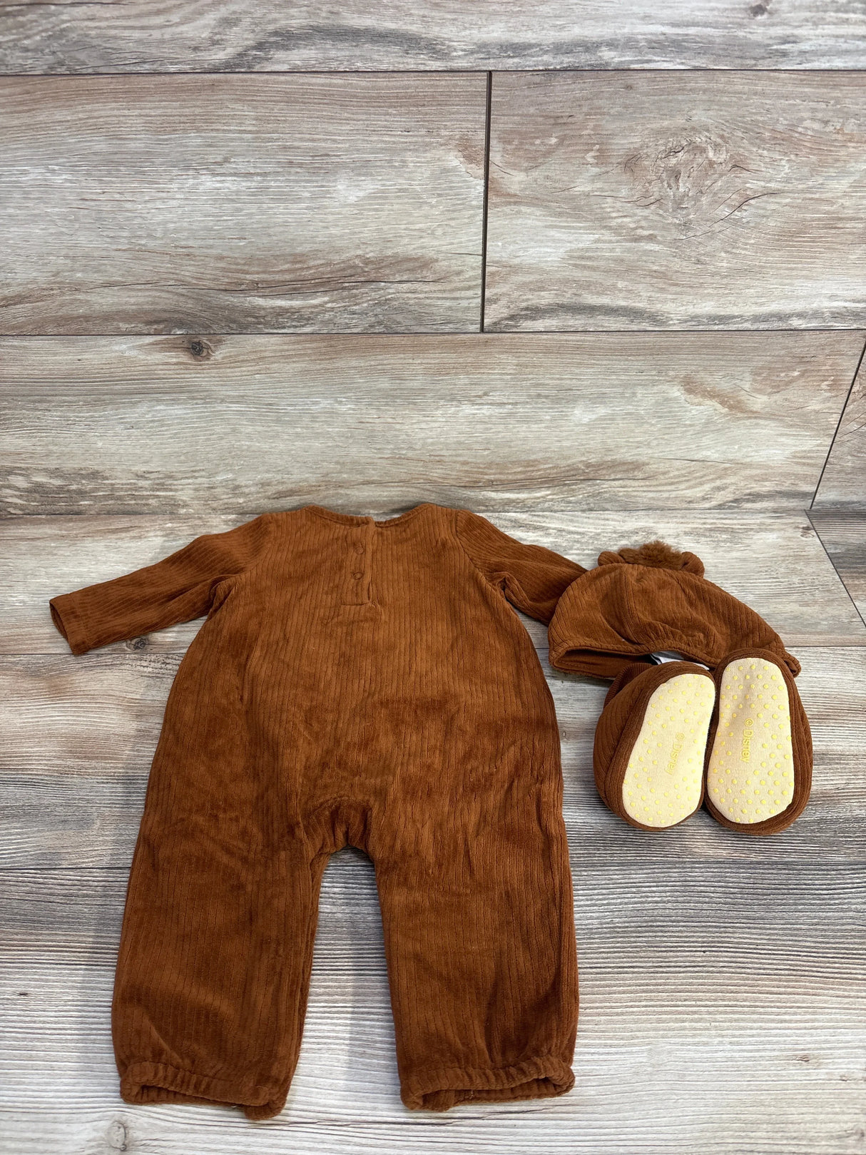 Brown corduroy baby romper with matching hat and booties on wood floor