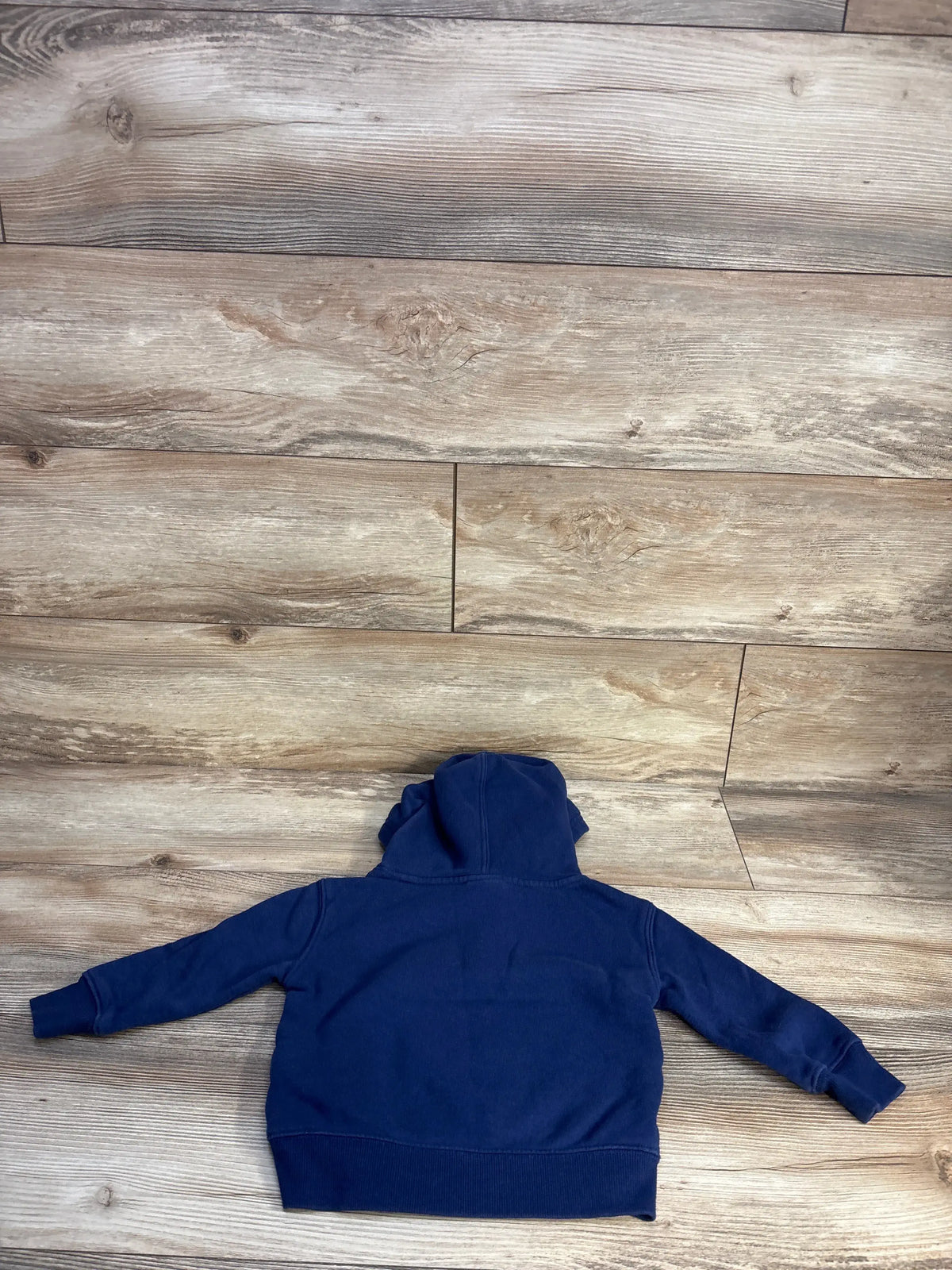 Back view of a navy blue Champion pullover hoodie for toddlers, size 2T, on a wood floor.