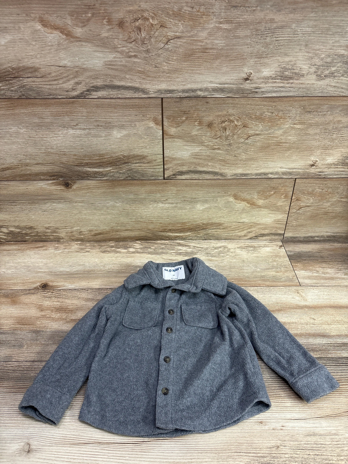 Front view of Old Navy grey fleece button-up jacket showcasing button front and two chest pockets with wood floor background