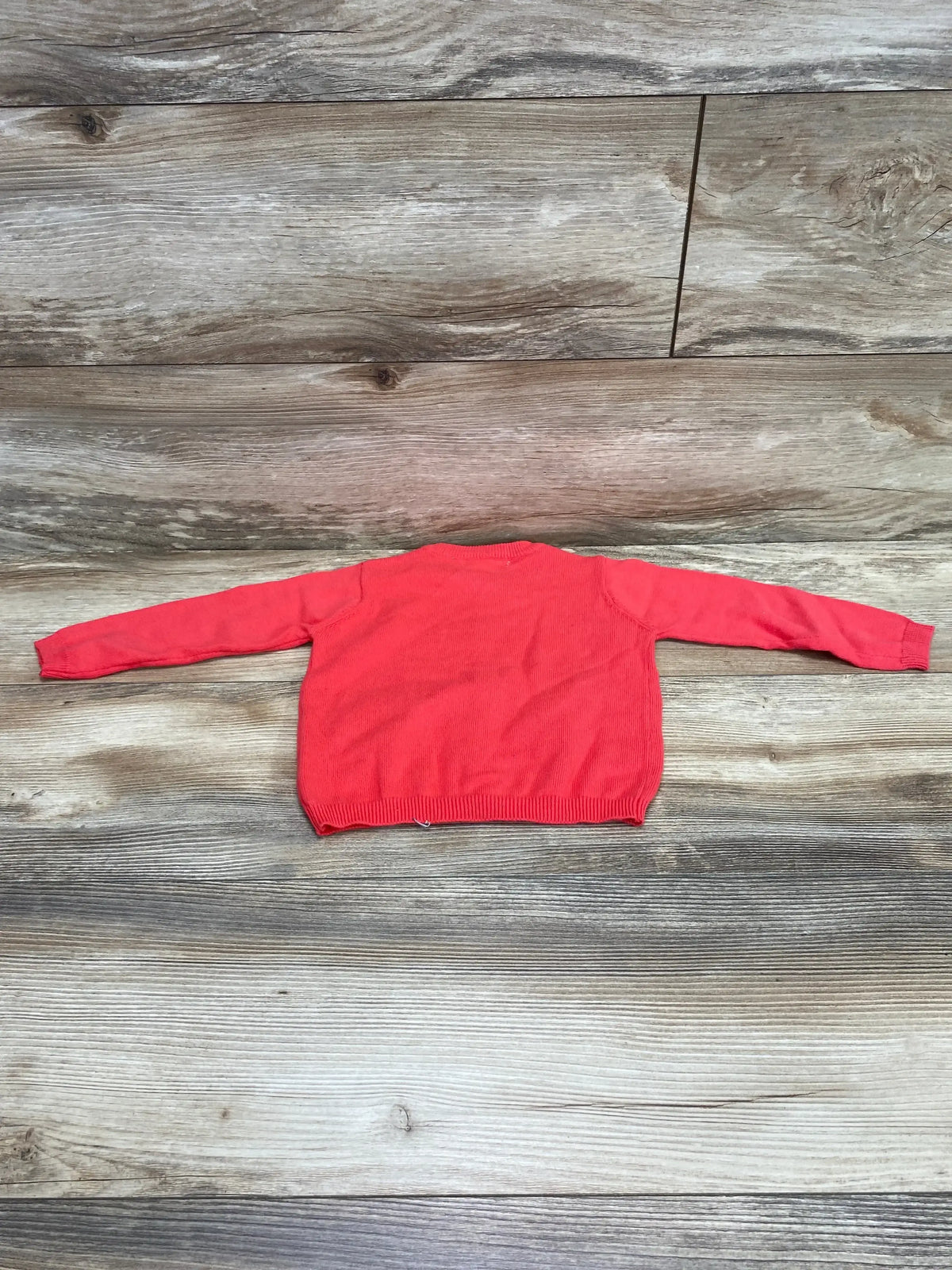 Back view of pink toddler cardigan, size 12 months, showing long sleeves and ribbed hem on wood plank background