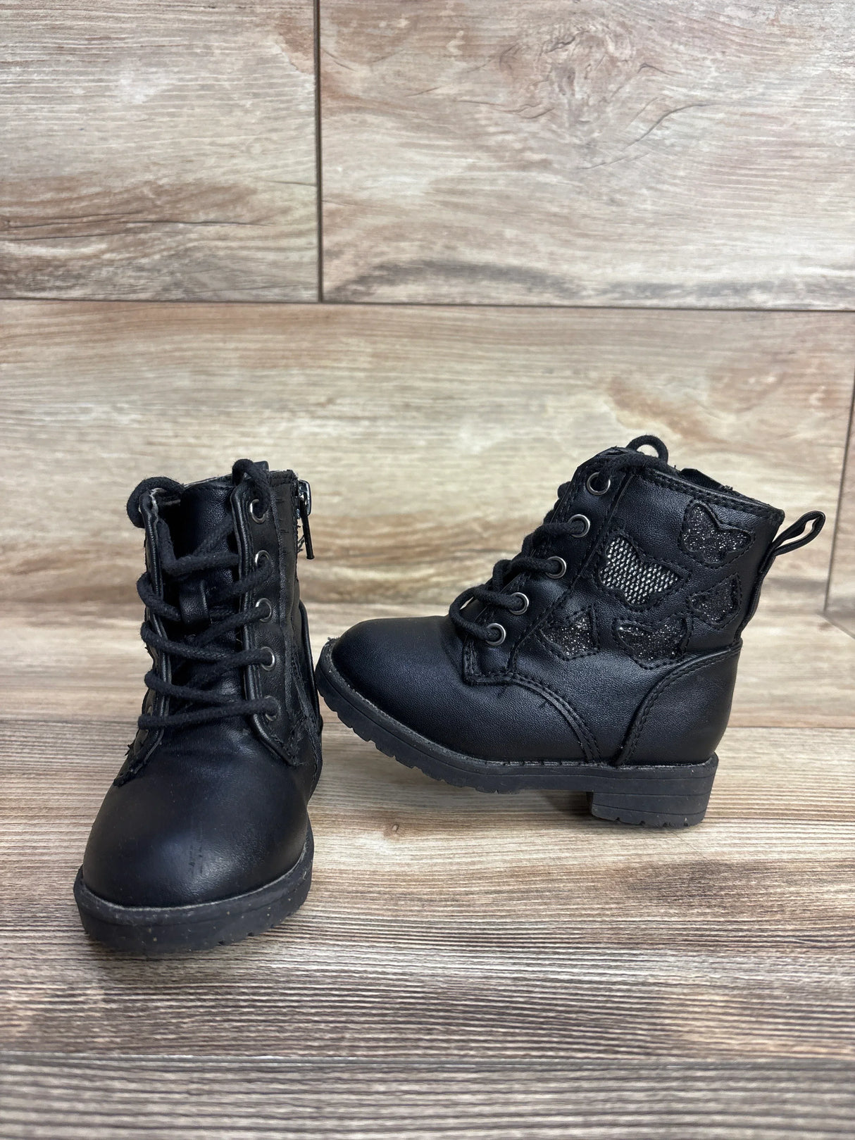 Front and side view of black Sugar faux leather toddler boots size 5C showing butterfly appliques and lace-up front on wooden floor