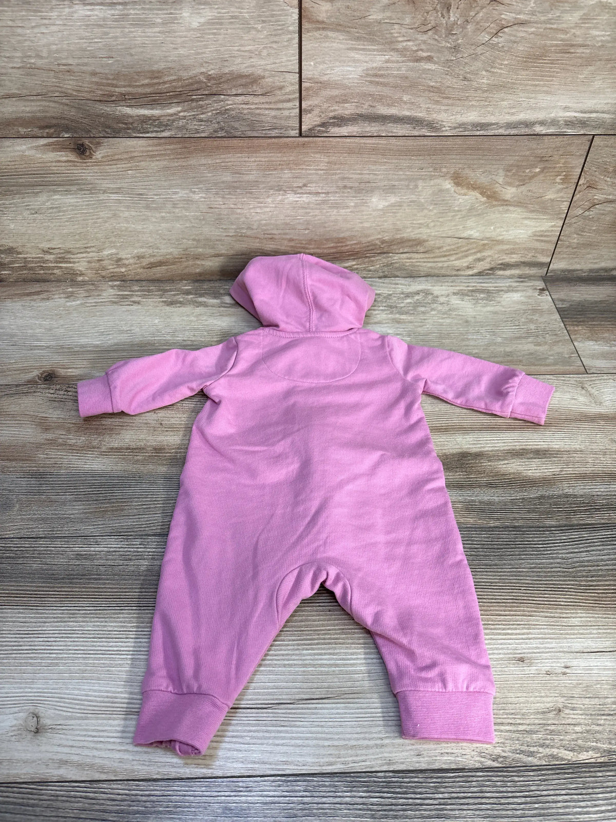 Back view of Nike pink hooded coverall showcasing long sleeves and ribbed cuffs with a wood-look background
