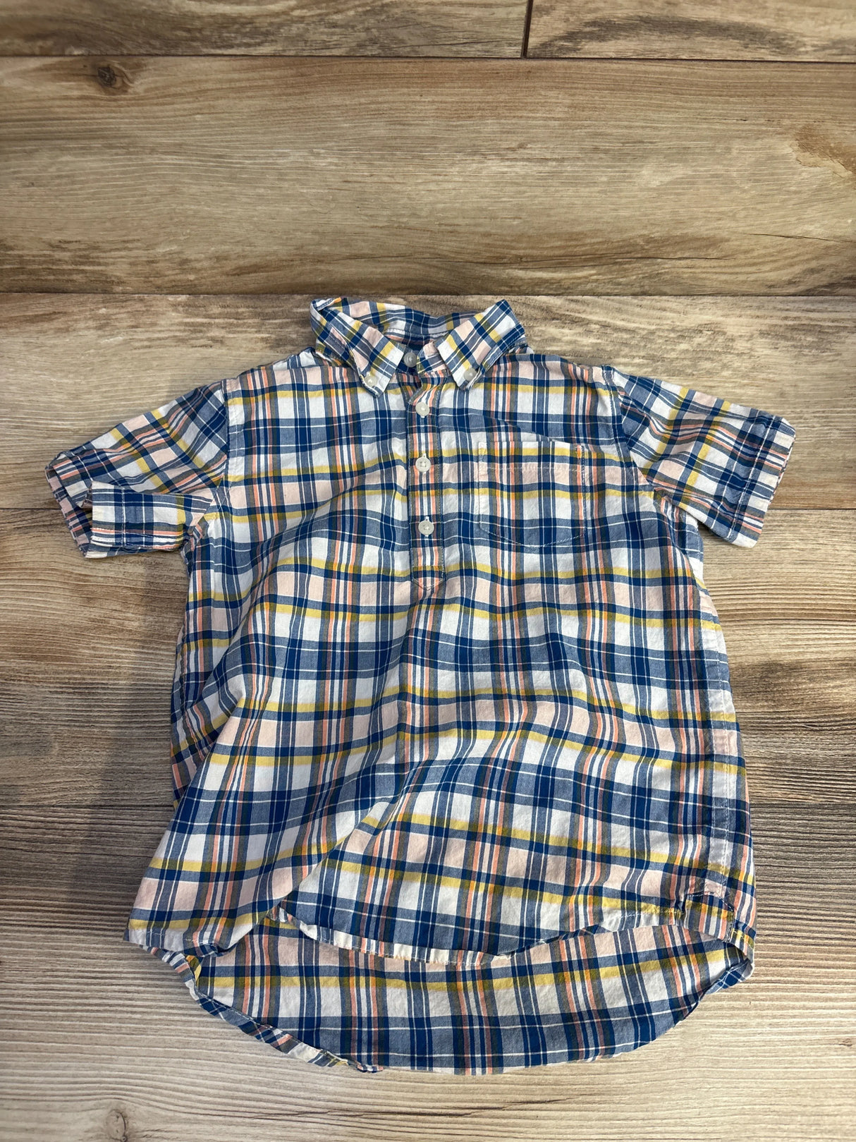 Short-sleeve button-up plaid shirt with blue, pink, yellow, and white colors on wooden background
