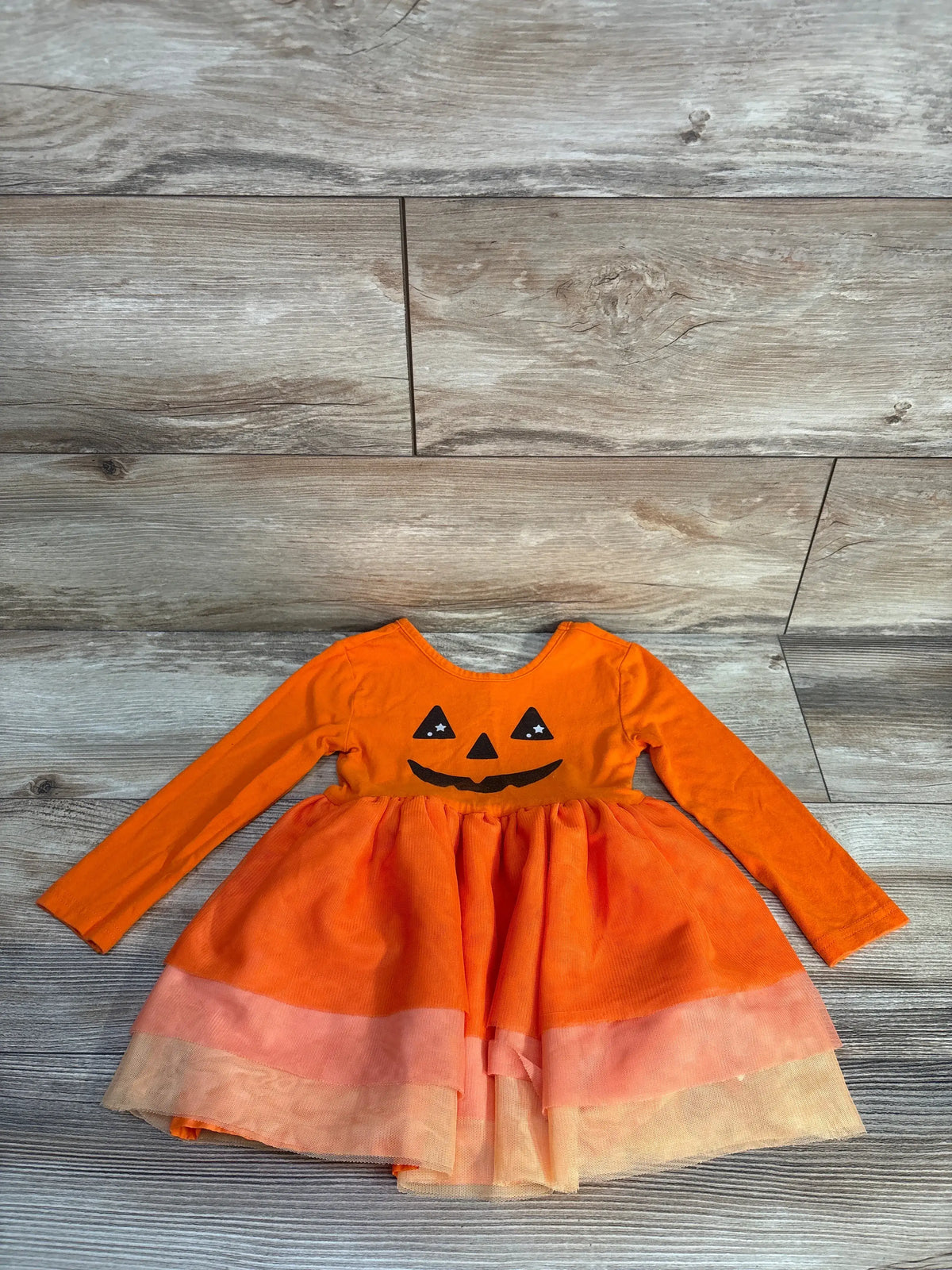 Front view of pumpkin orange toddler tutu dress showcasing jack-o-lantern face, long sleeves, and layered skirt on wood