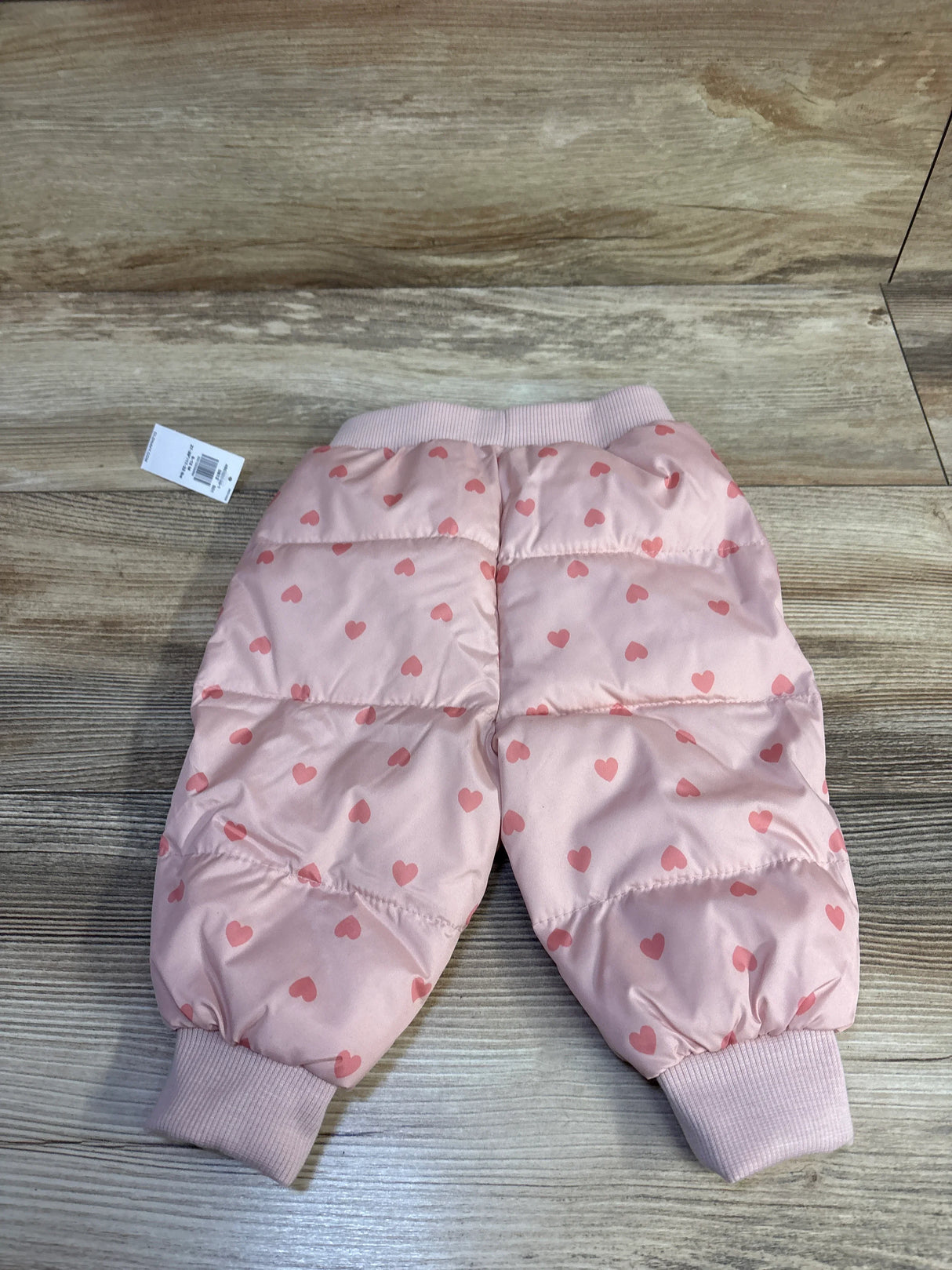 Flat-lay of Old Navy pink water-resistant quilted tapered pants with heart print and ribbed cuffs on wood background