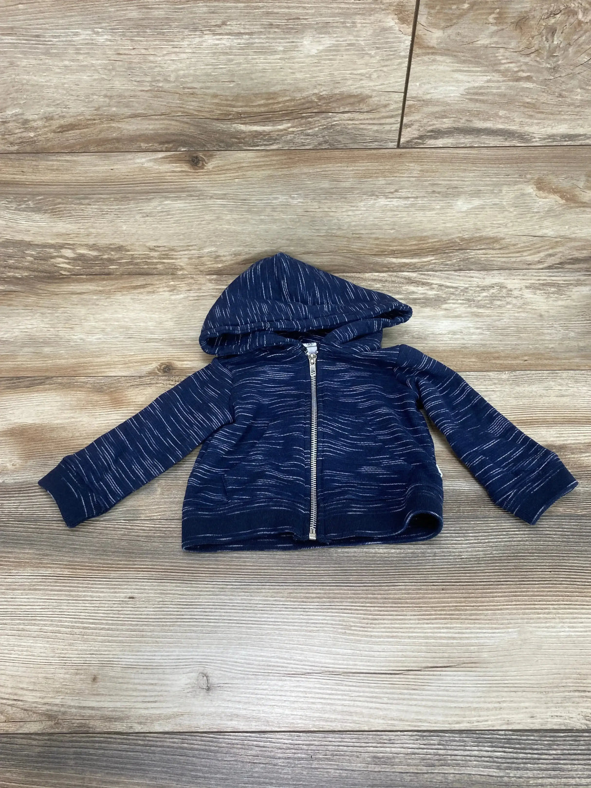 Flat lay of baby navy full zip hoodie showcasing hood, front zipper and white heathered pattern with light wood background