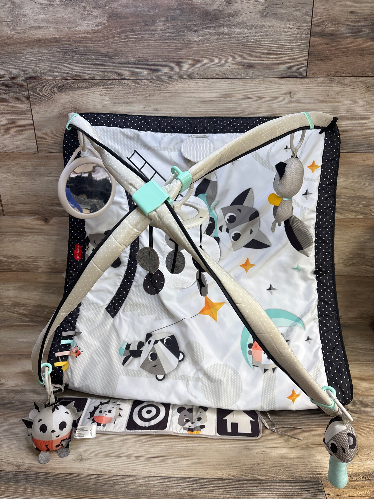 Top-down view of Gymini play gym showcasing crossed arches, hanging black-and-white toys and mirror on wood floor