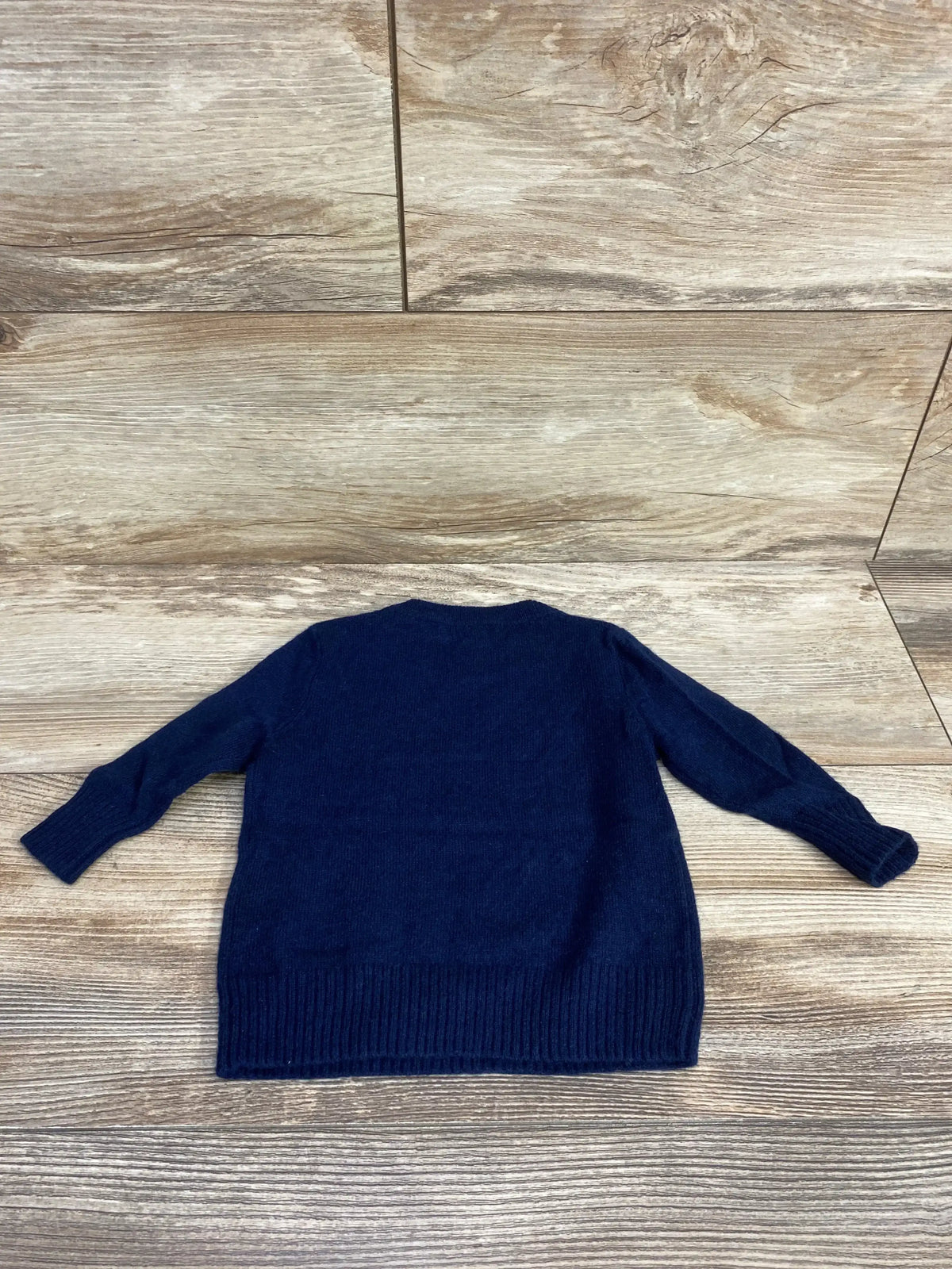 Back view of J.Crew baby cashmere sweater (size 3–6M) in navy showing long sleeves and ribbed hem on wooden floor