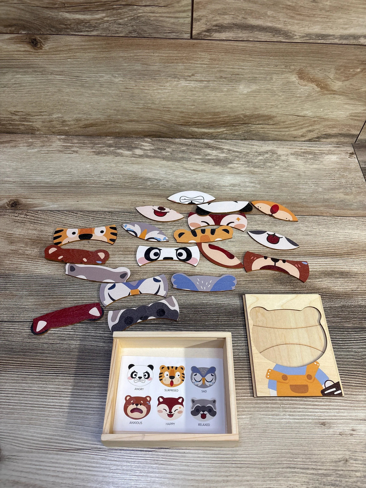 Top-down view of Animal Emotions wooden puzzle box showing 18 animal face pieces beside the wooden tray on a light wood surface