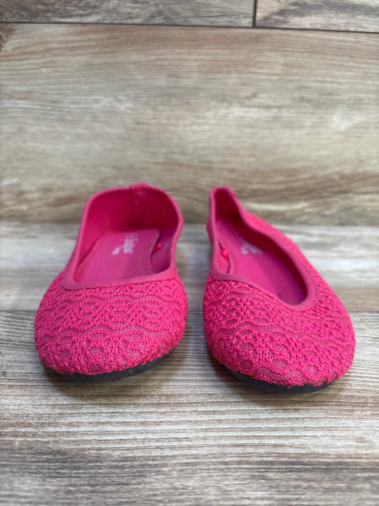 Pink lace toddler ballet flats with textured pattern on wooden floor