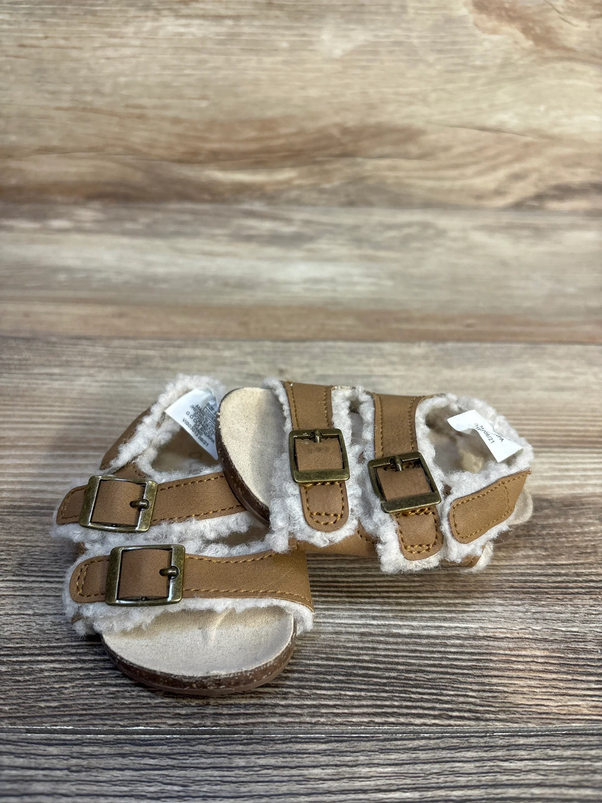 Tan toddler sandals with faux shearling lining and buckle straps on wooden background