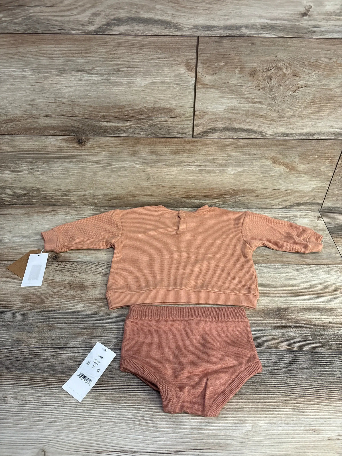 Orange long-sleeve baby sweater and matching knit diaper cover on wooden surface, tags attached
