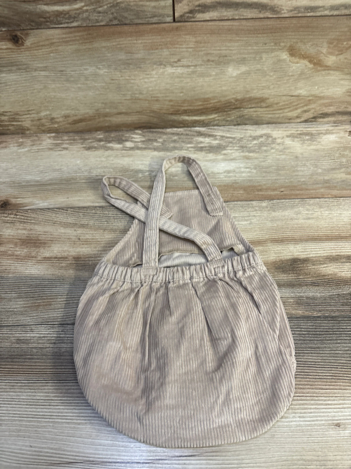 Flat lay of beige corduroy bubble shortalls size 12M with crossed back straps and elastic waist on wood surface