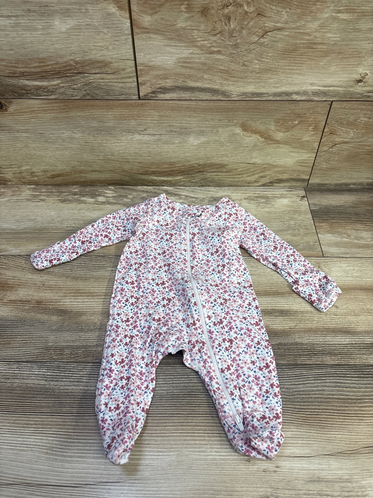 Front view of white Just One You floral sleeper with pink and blue flowers, front zipper, and enclosed feet on wood flooring