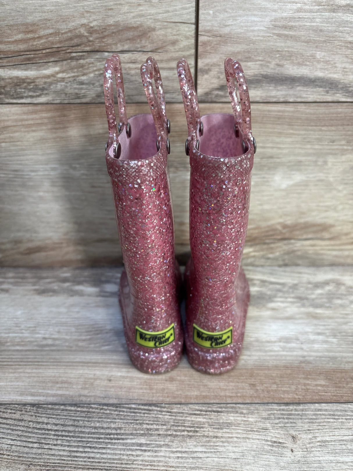 Pink glitter kids rain boots with handles, Western Chief brand, on wood background