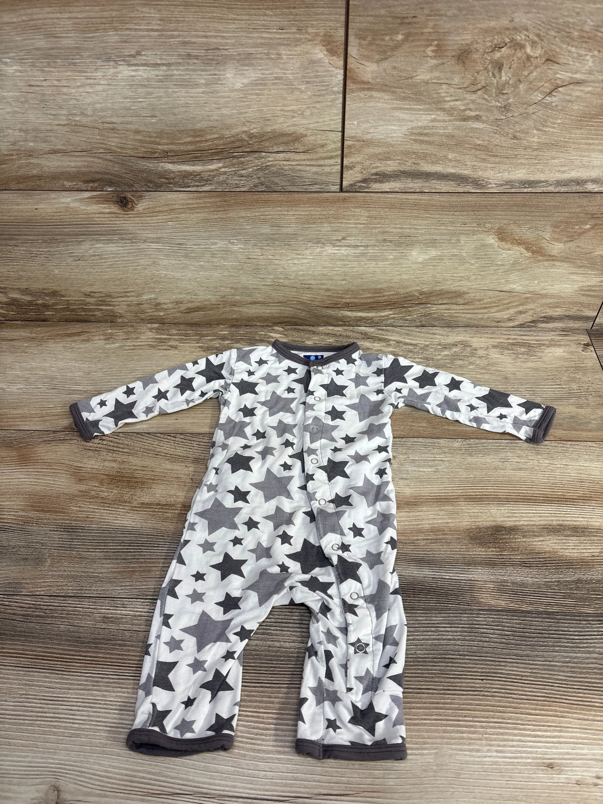 Baby onesie with gray and black star pattern, snap buttons, and dark trim on wood floor