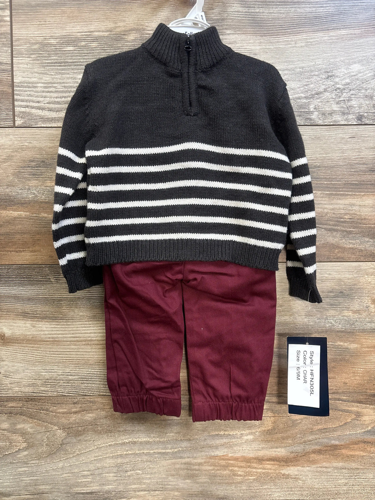 Front view of quarter-zip sweater and pants, black sweater with white stripes and maroon pants, size 6-9M tag on wood