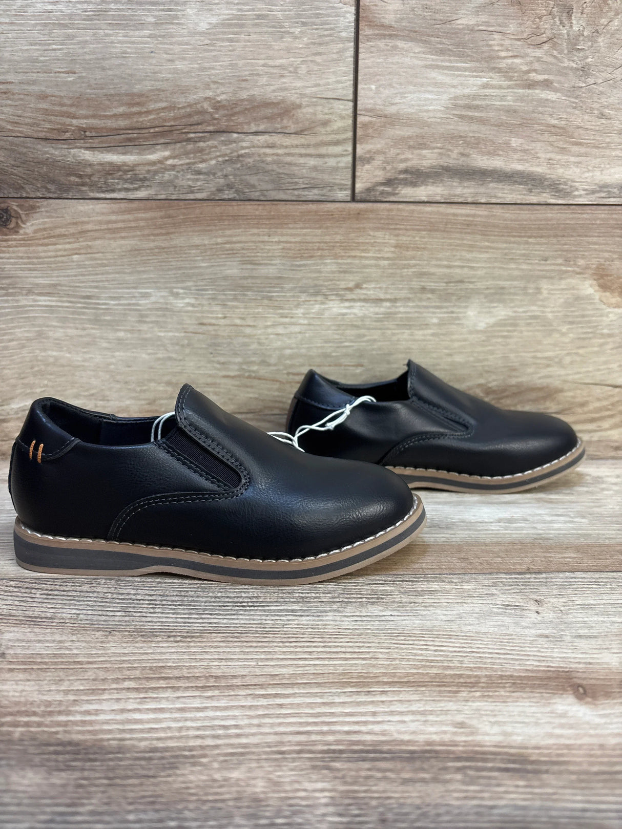 Black leather slip-on kids dress shoes with brown soles on wooden background
