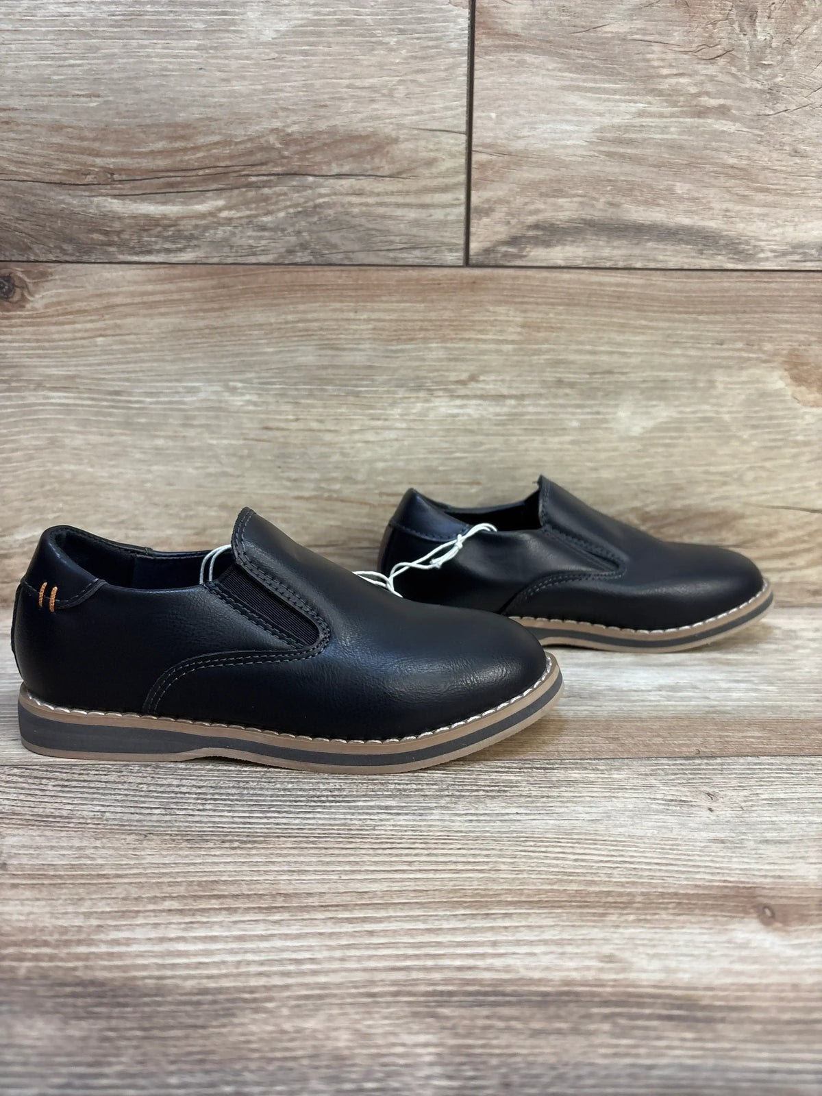 Black leather slip-on kids dress shoes with brown soles on wooden background