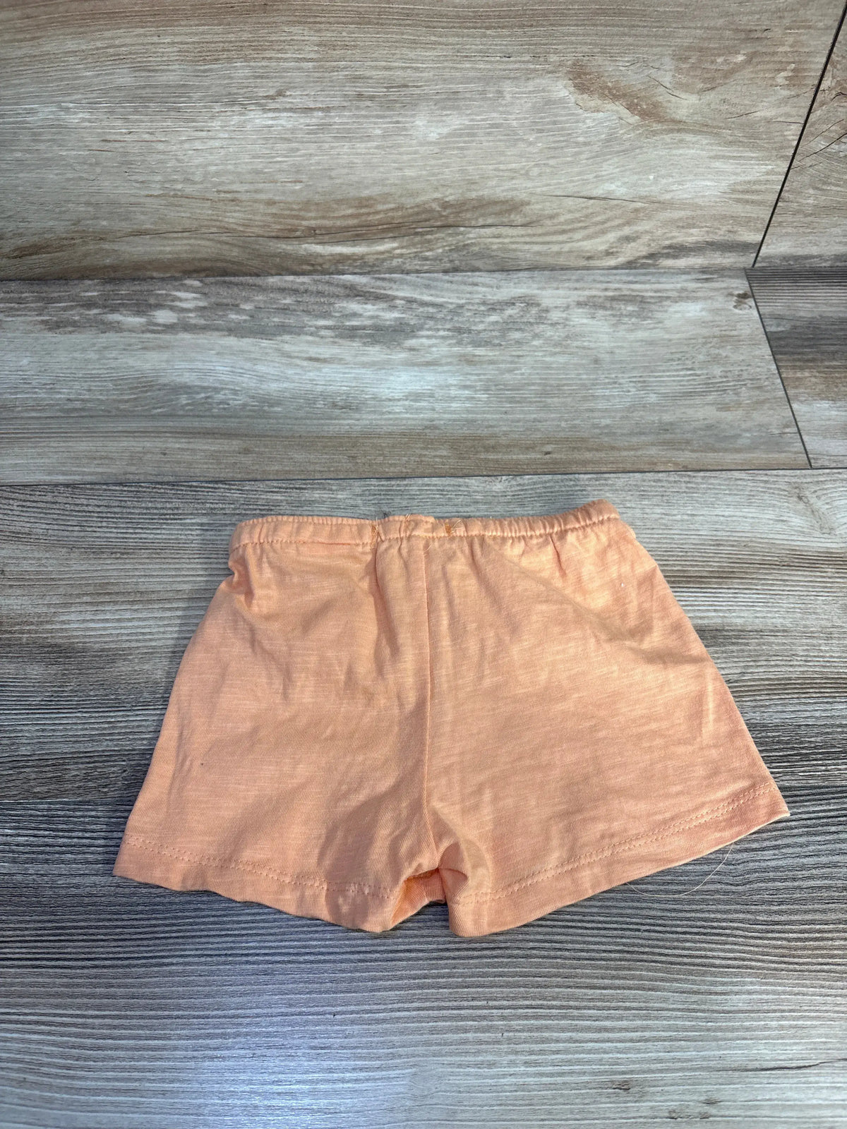 Front view of orange Sinsay baby shorts (3-6 months) showing elastic waistband and cotton knit fabric on light wood background