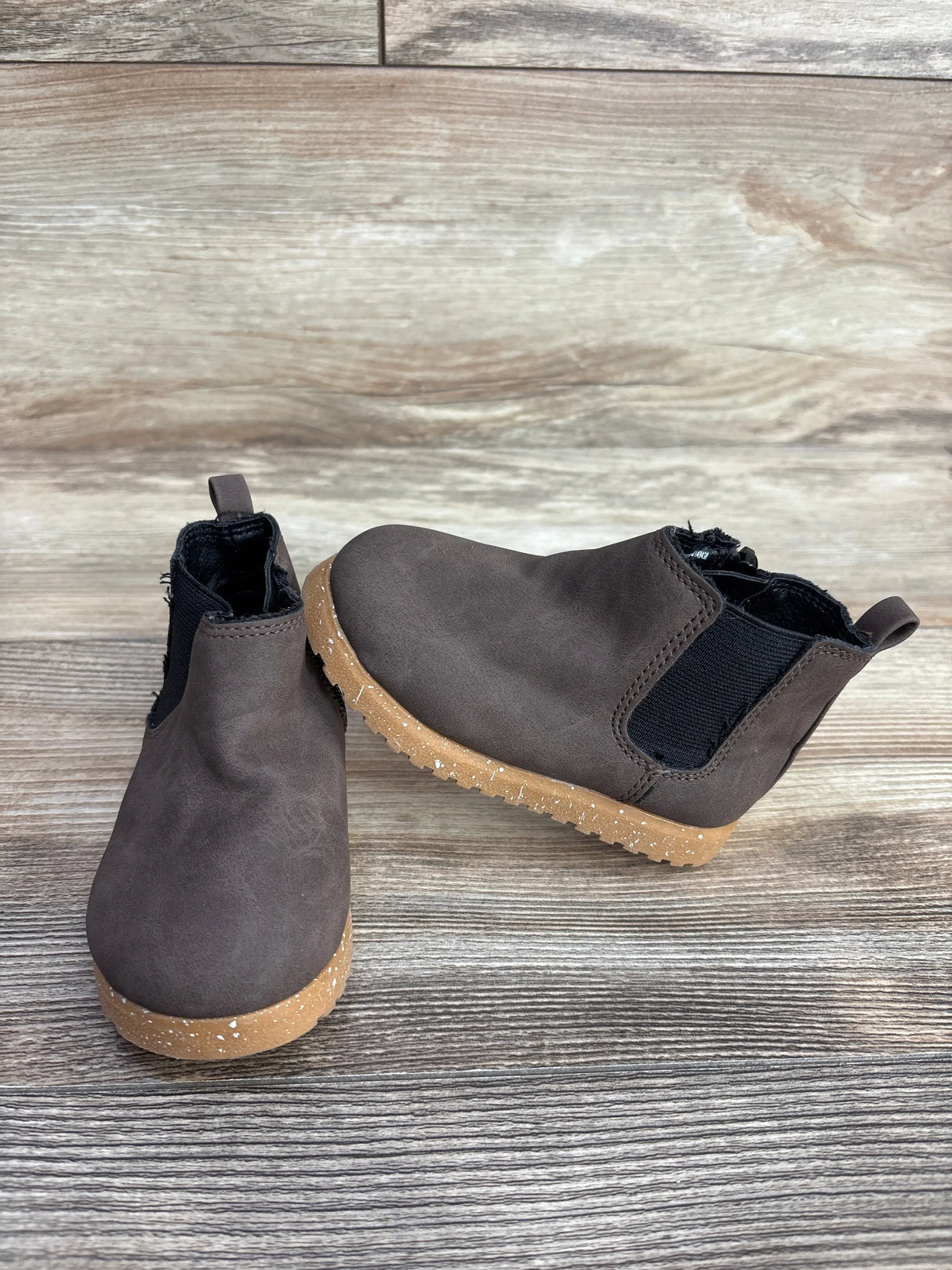 Pair of brown toddler Chelsea boots with tan speckled soles on wooden surface