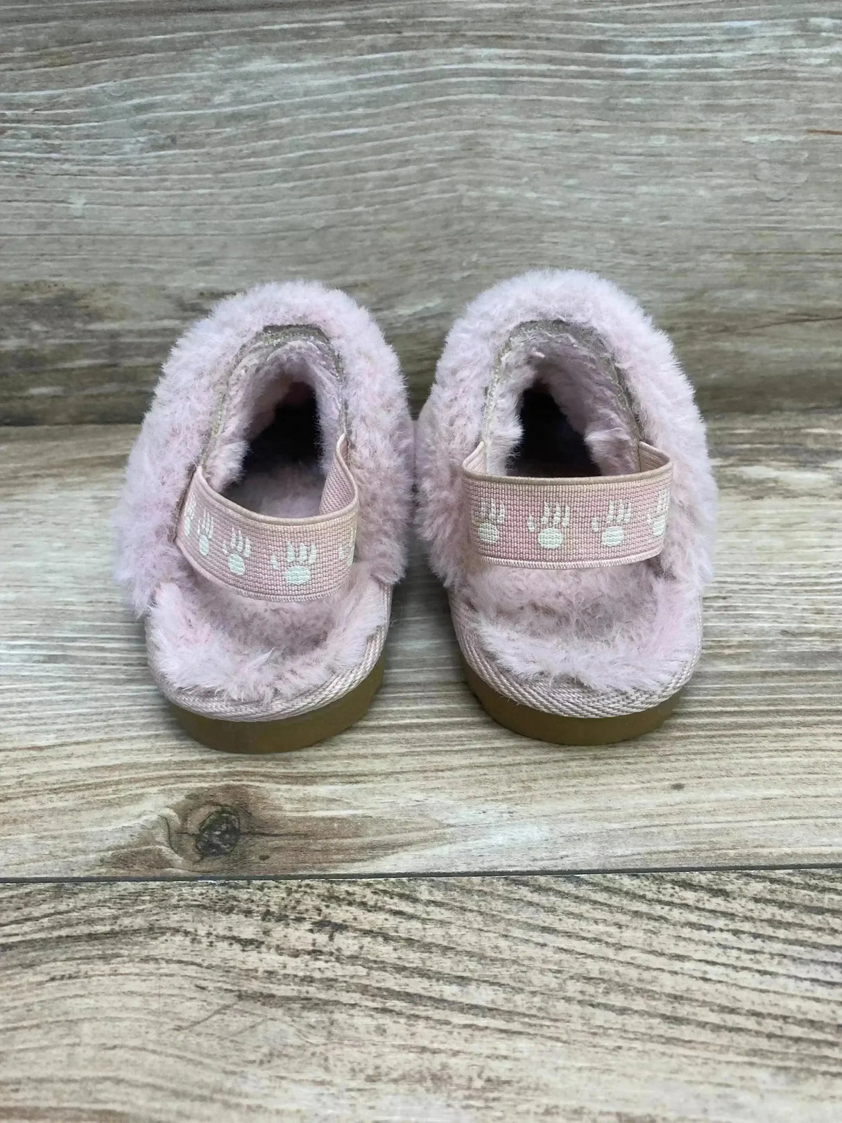 Back view of light pink Bearpaw Rebecca suede slippers showing sheepskin lining and paw-print elastic strap on wooden floor