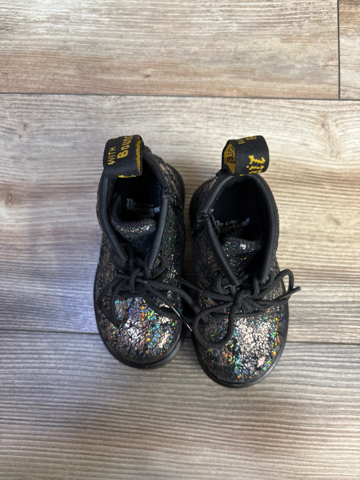 Overhead view of Dr. Martens 1460 kids boots with crinkle metallic iridescent finish and yellow pull tabs on wood floor