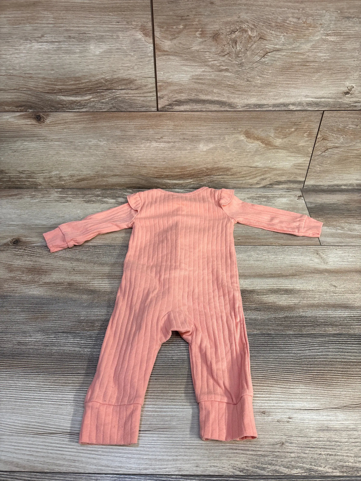 Front view of Carter’s coral ribbed coverall for 6 months, showcasing ruffle sleeves and footless legs on a wood-look floor