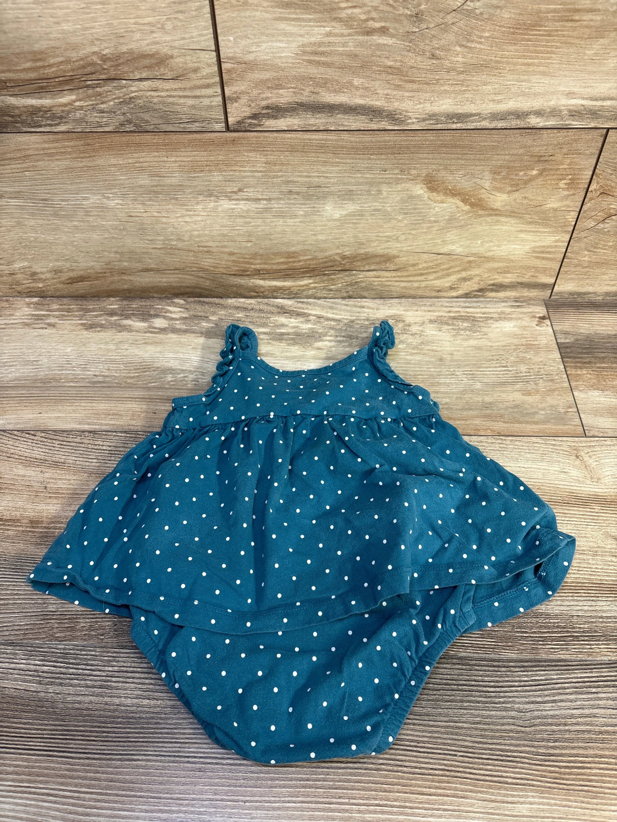 Flat lay of teal polka-dot bodysuit dress showing ruffled shoulder straps and gathered skirt on wood floor, size 18 months