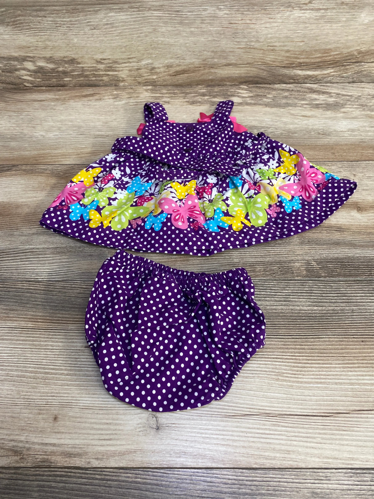 Flat lay of purple polka-dot baby dress and bloomer showing colorful butterfly print and ruffled skirt on wood background