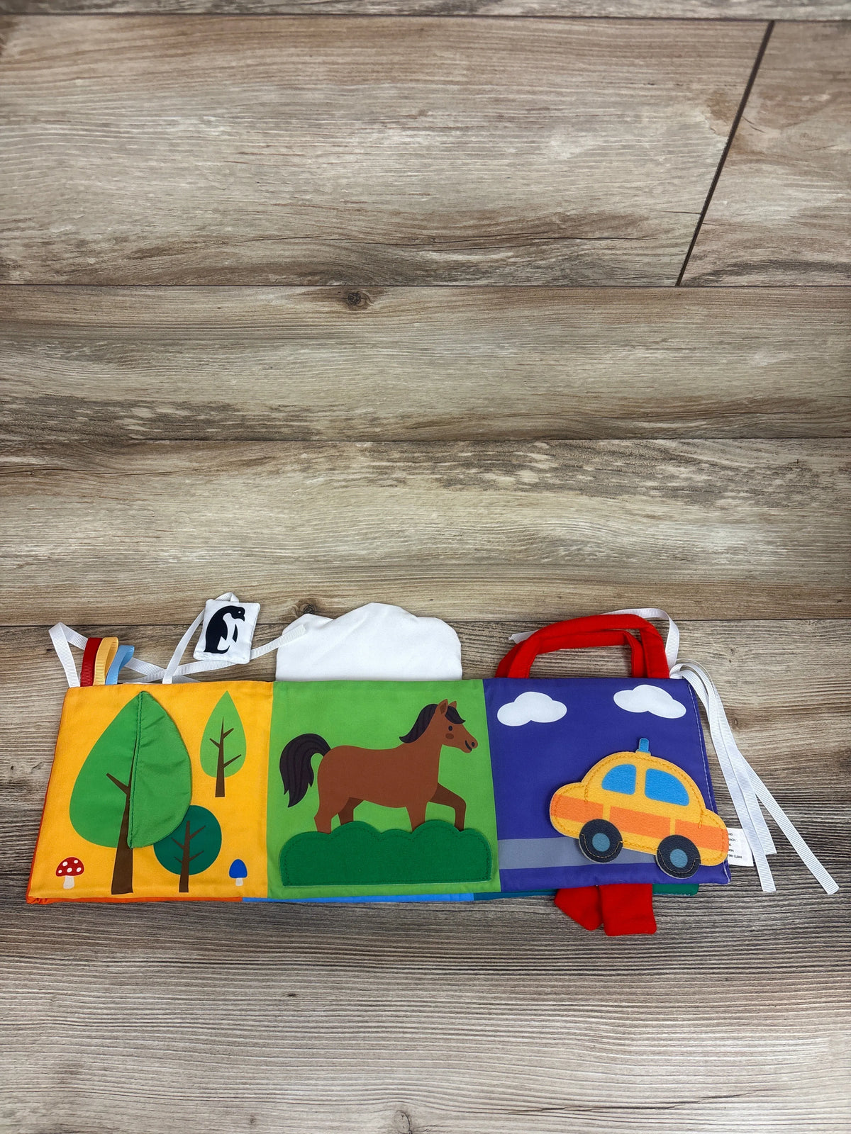 Top view of HahaLand High Contrast Tummy Time Cloth Activity Book showcasing colorful forest, horse, and car scenes on a wood surface