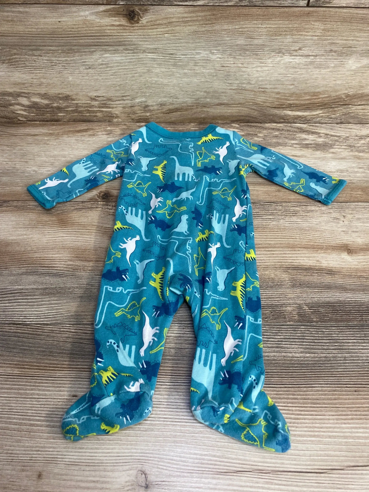 Flat lay of blue Carter’s footed baby sleeper size 3M showing multicolor dinosaur print on wood background