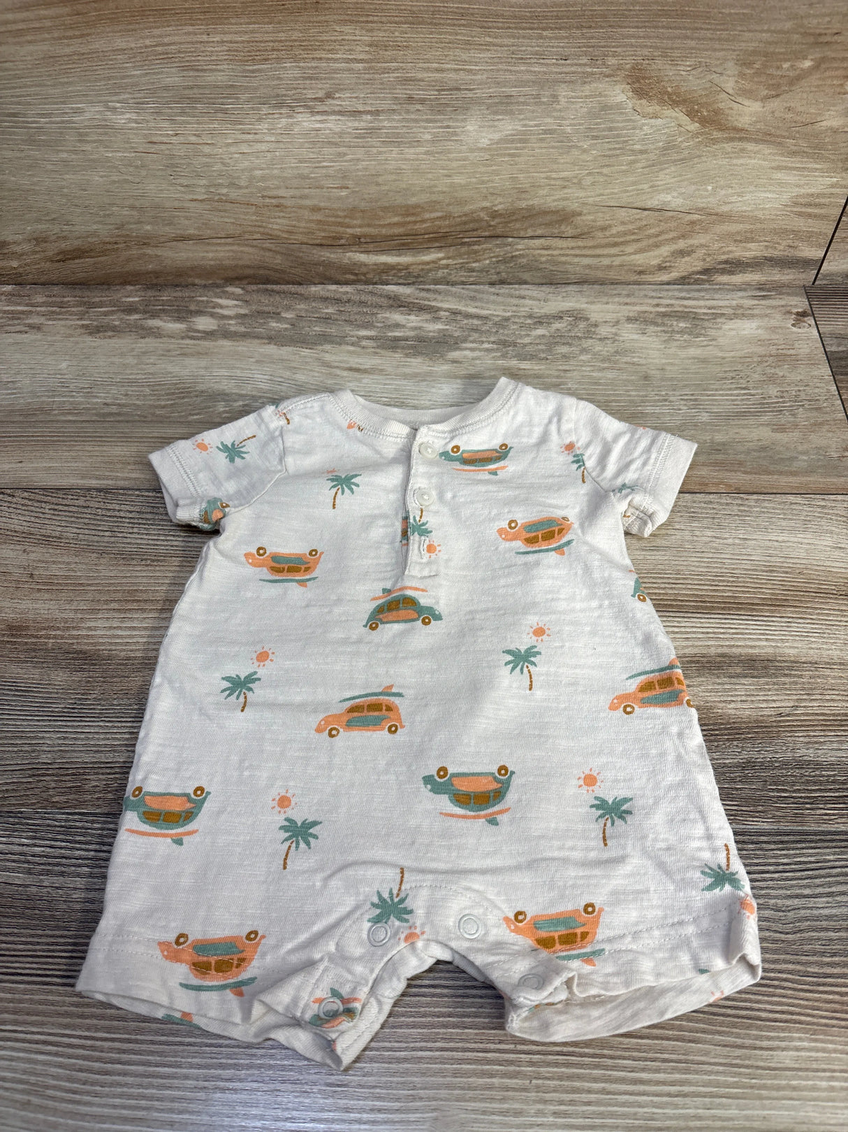 Front flat-lay of ivory baby henley shortie romper showcasing orange and teal car print, front henley button placket and snap crotch on wood background