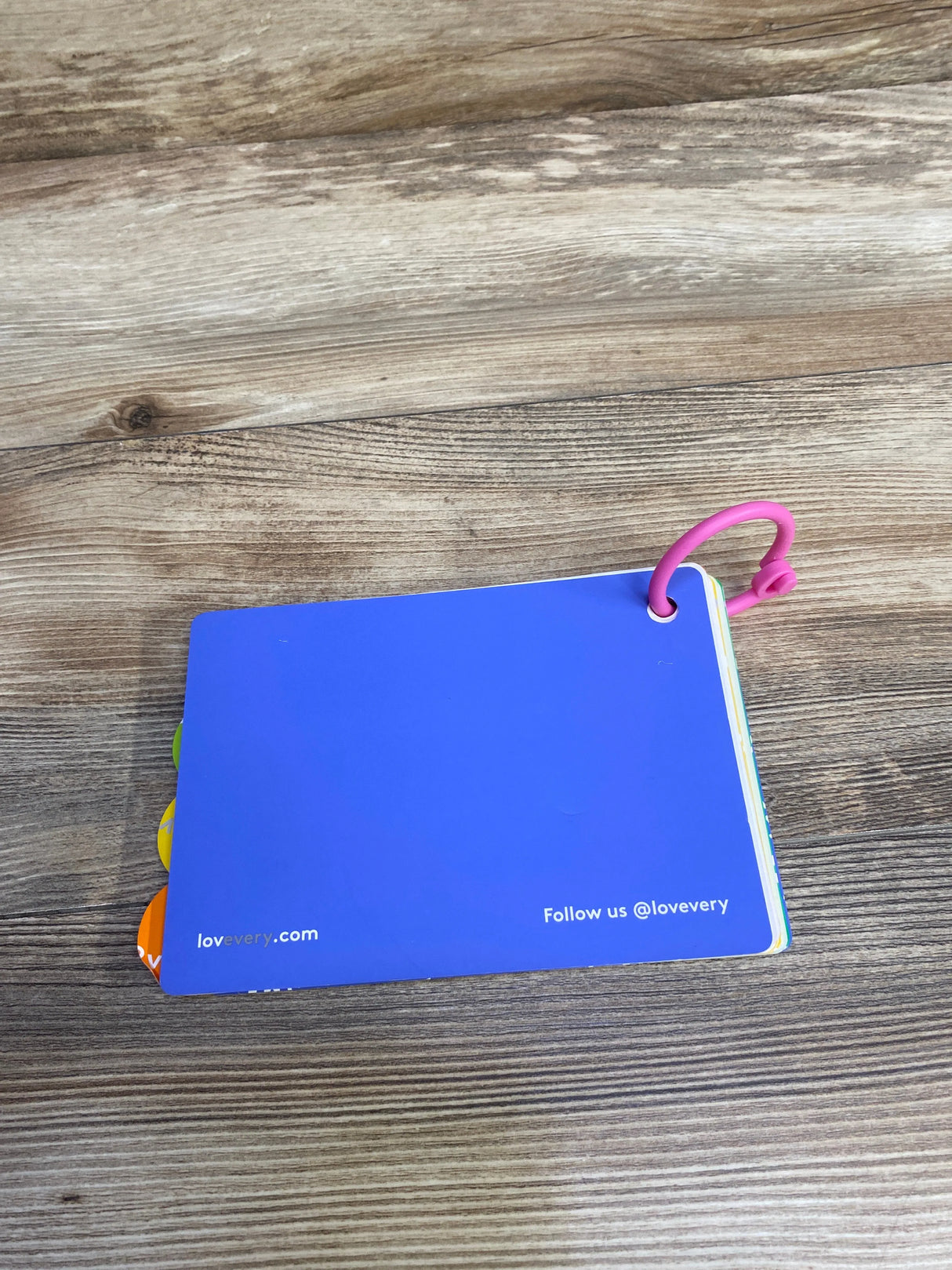 Blue Lovevery board book with pink ring on wood surface, colorful tabs visible