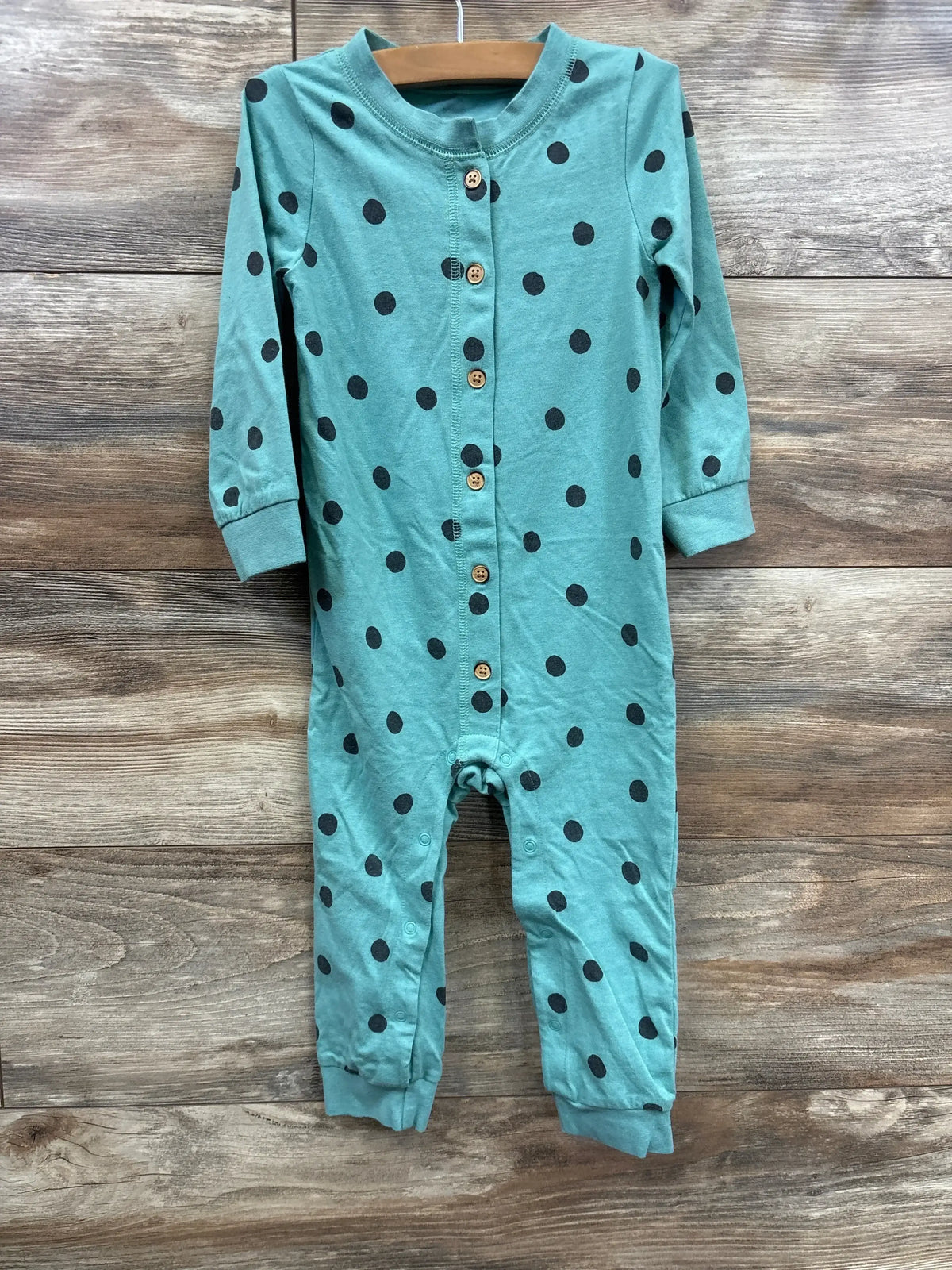 Teal baby romper with black polka dots and wood buttons on wooden background