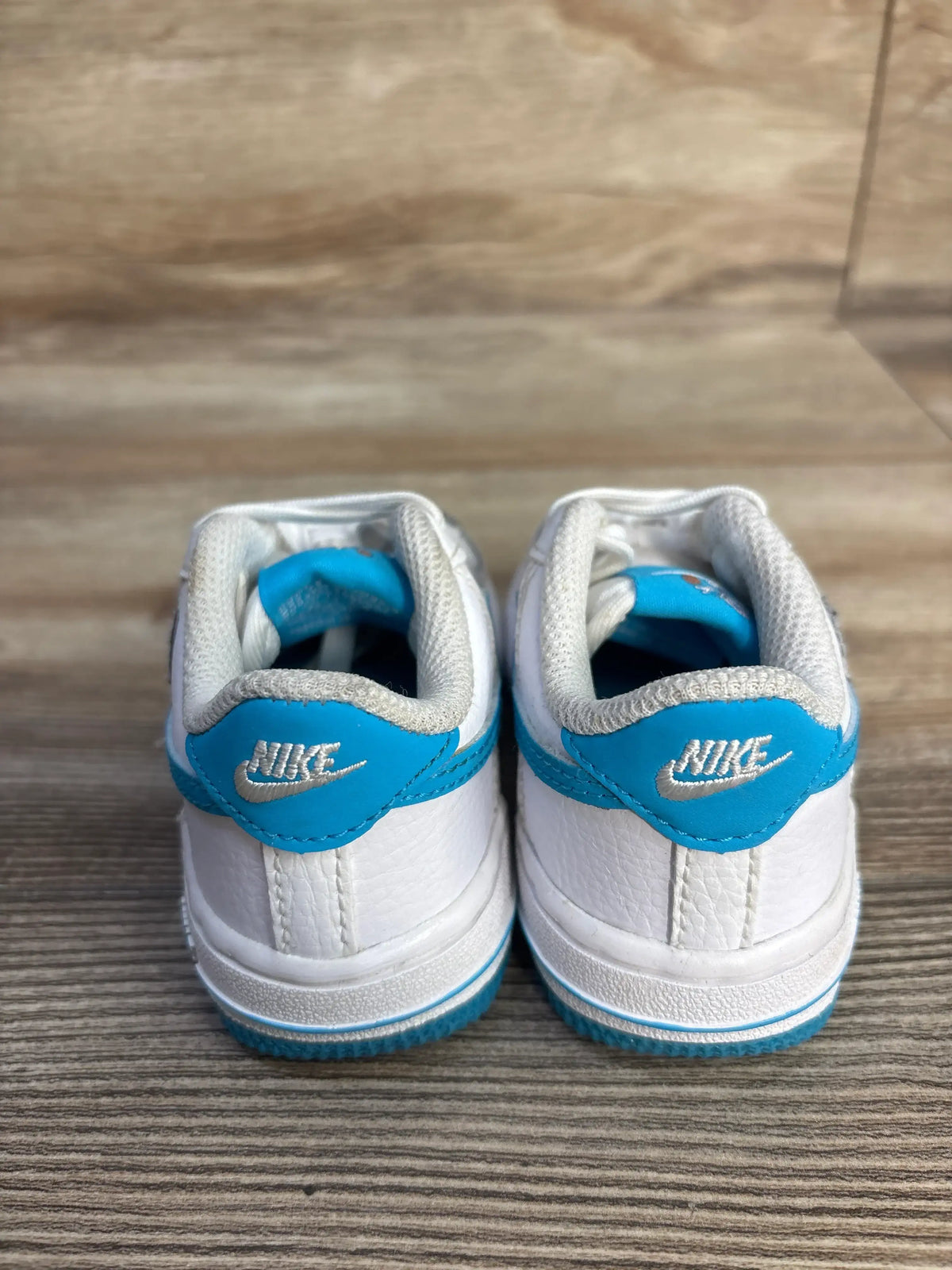 Rear view of Nike Air Force 1 TD x Space Jam Hare sneakers with Light Blue Fury heel overlays on wood floor