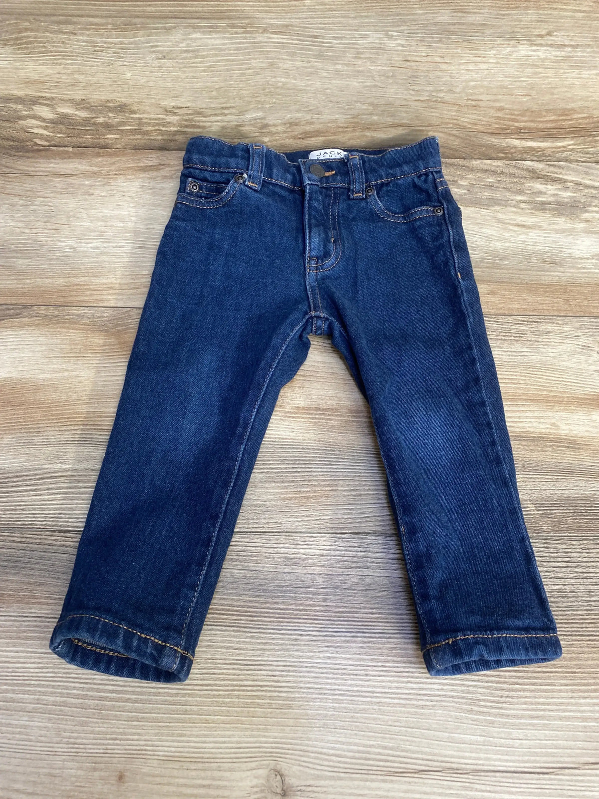 Flat lay of Jack denim slim jeans showcasing dark wash blue with five pocket styling on wood plank floor