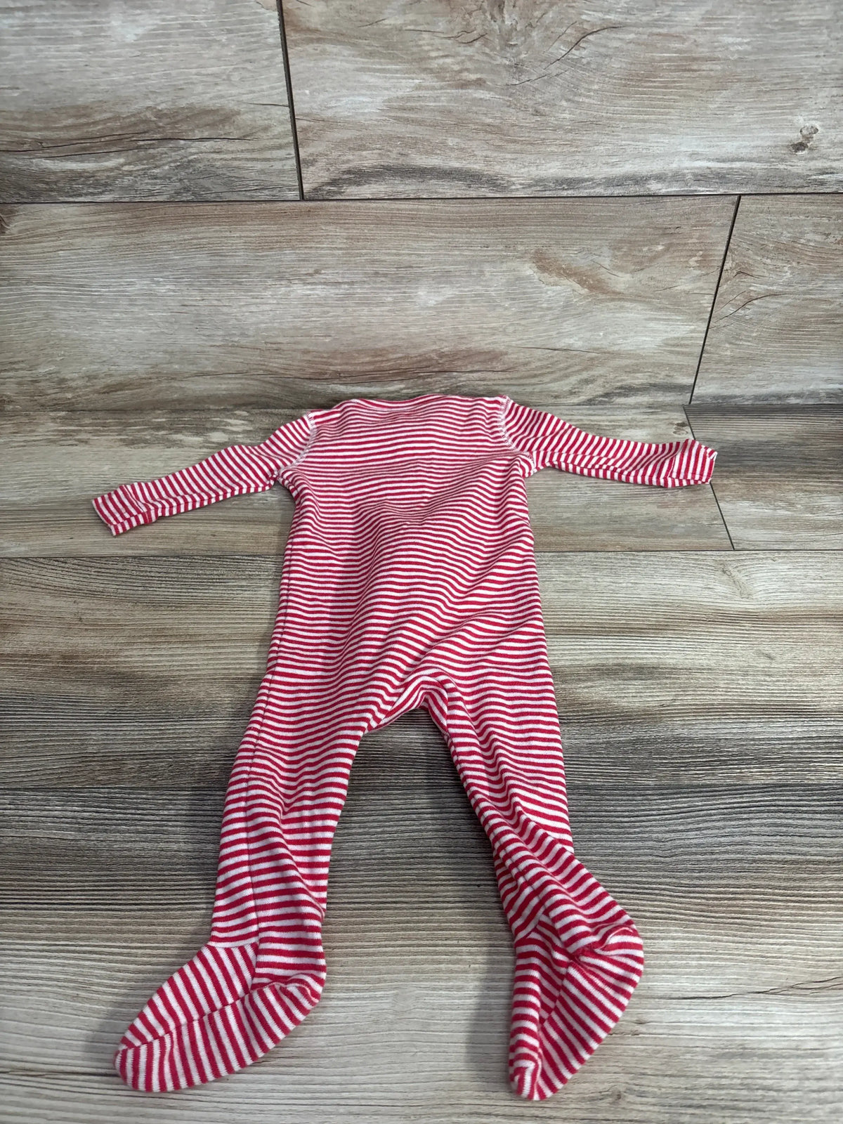 Top-down view of Primary organic red and white striped footed sleeper showing long sleeves and built-in feet on a light wood floor