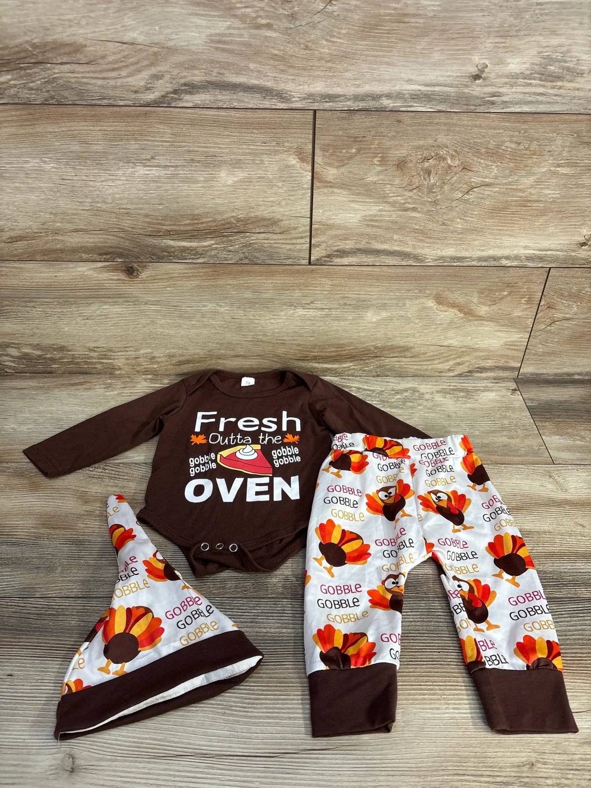 Thanksgiving baby outfit with brown bodysuit saying Fresh Outta the Oven and white pants, hat with colorful turkey print