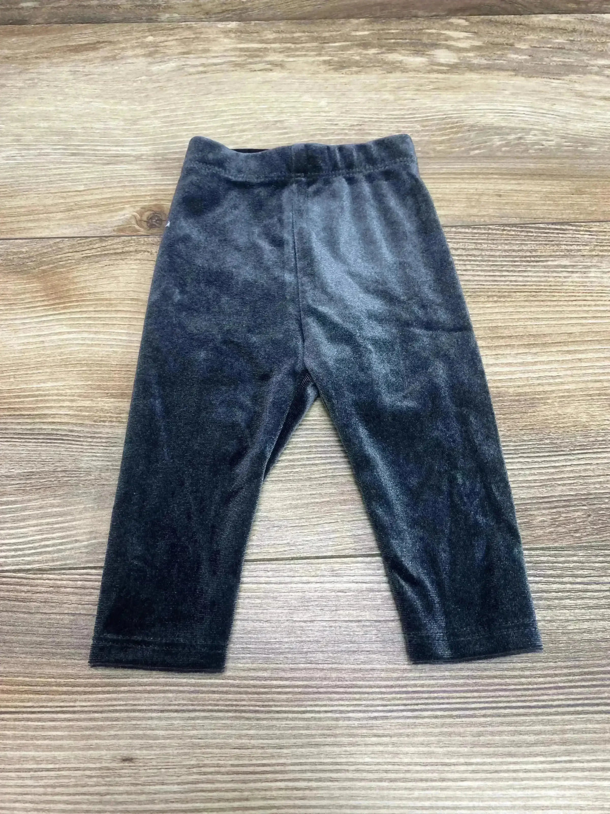 Flat-lay of newborn black velour leggings showing elastic waistband and soft velour texture on light wood background
