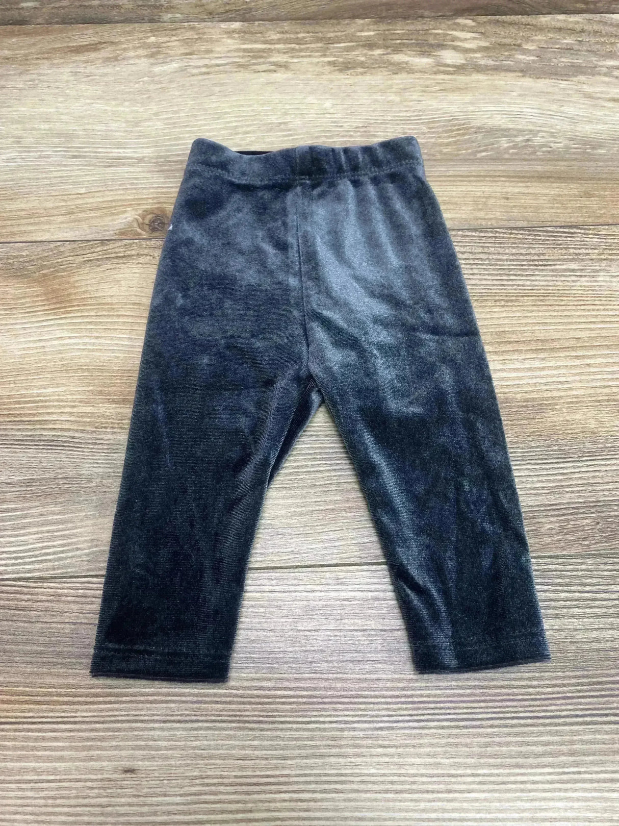 Flat-lay of newborn black velour leggings showing elastic waistband and soft velour texture on light wood background