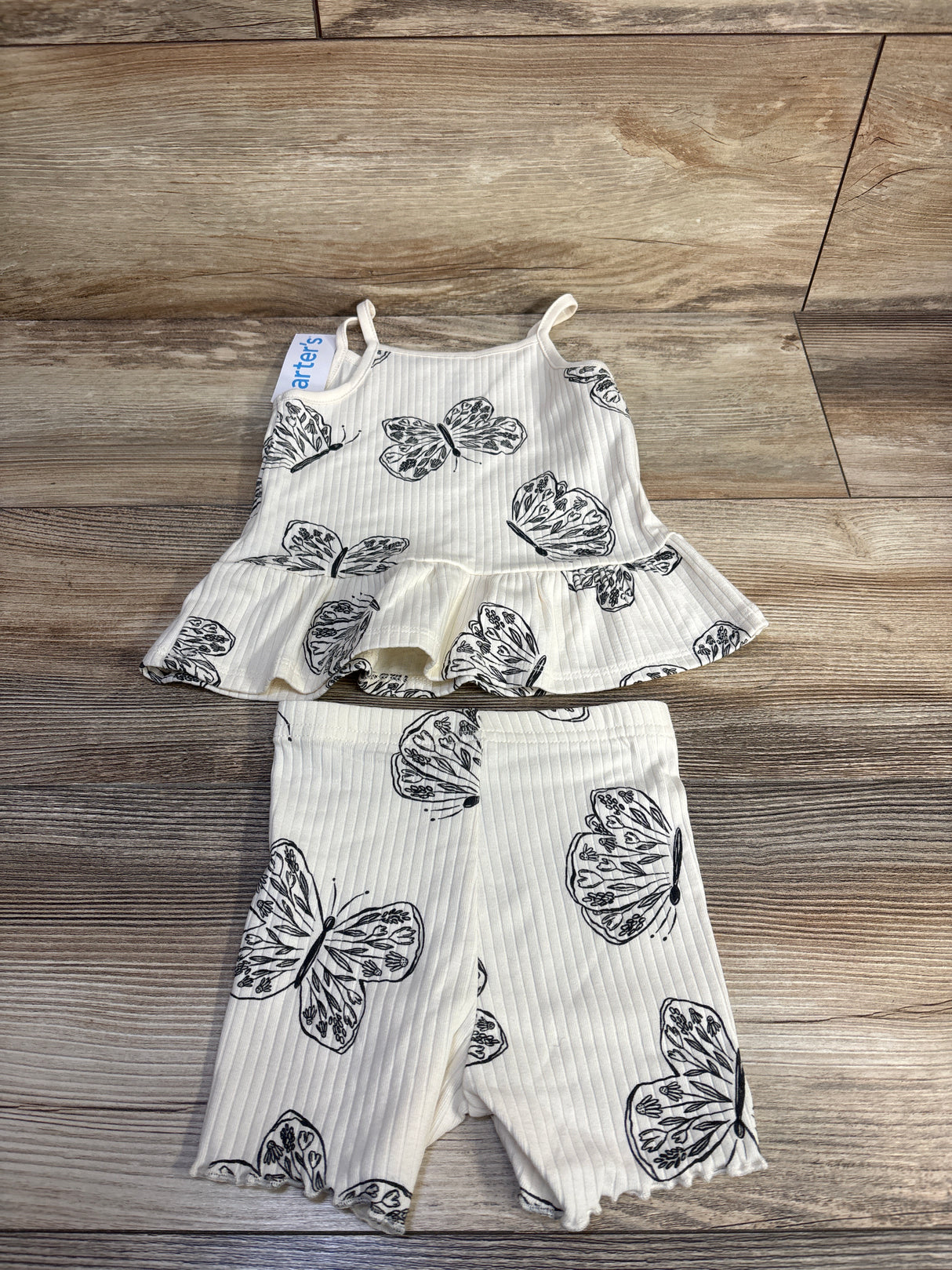 Flat lay of Carter's cream 2-piece ribbed tank and shorts set showing black butterfly print and ruffle hem on wood background