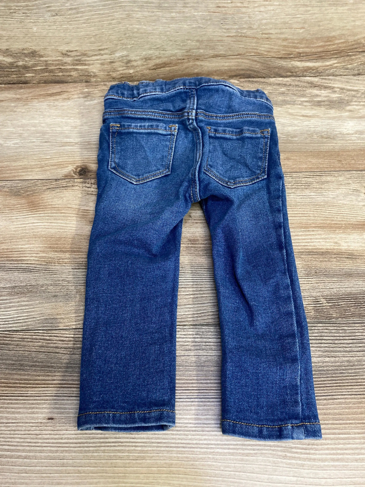 Back view of blue Old Navy toddler skinny jeans 18-24 months showing elastic waistband and back pockets on wood background