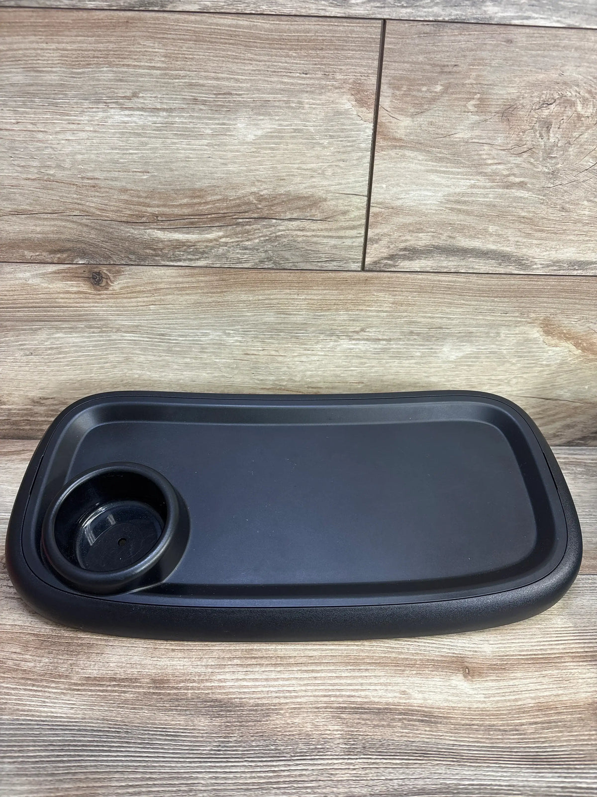 Top view of Leadigol stroller snack tray with cup holder showcasing a single recessed cup holder and raised tray edges on a wood-look floor