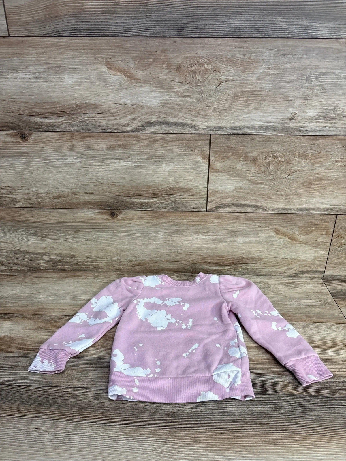 Front of Girls Grayson Mini Puff Sleeve sweatshirt in pink with white splatter, showing puff sleeves and ribbed hem on wood background