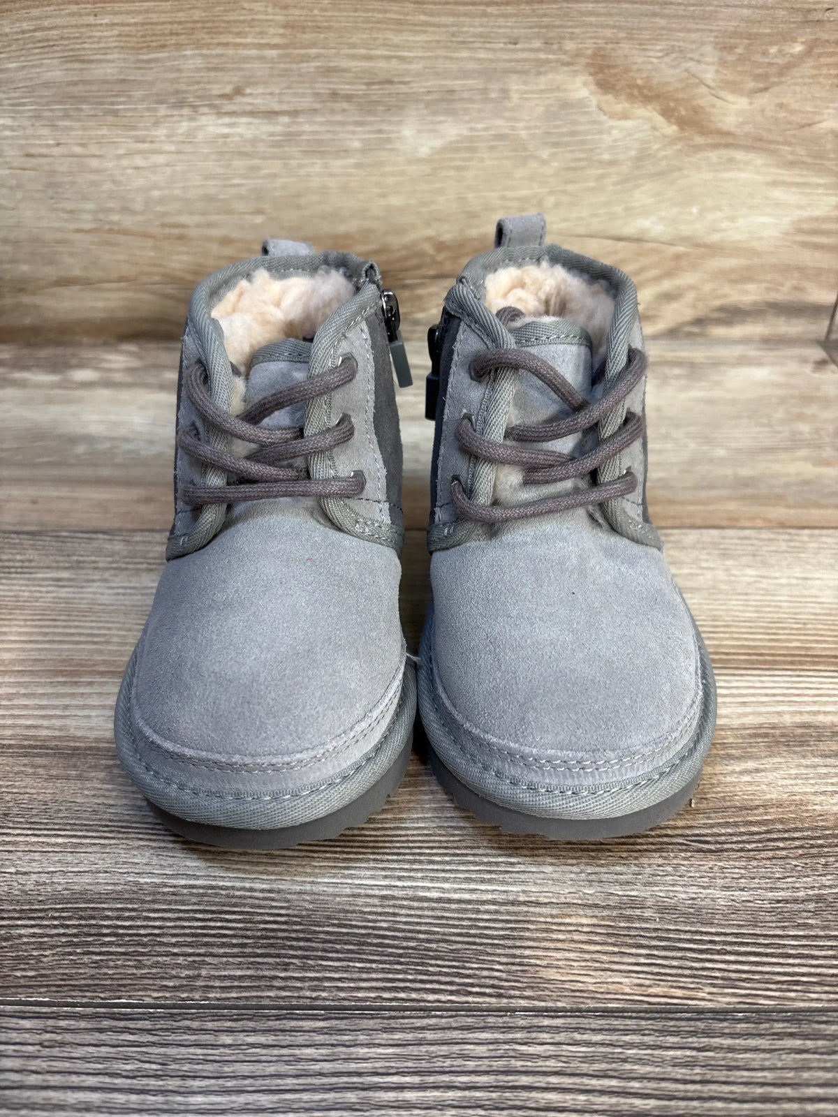 Front view of Ugg Neumel II toddler boots in grey suede showcasing faux fur lining and laces on a wooden background