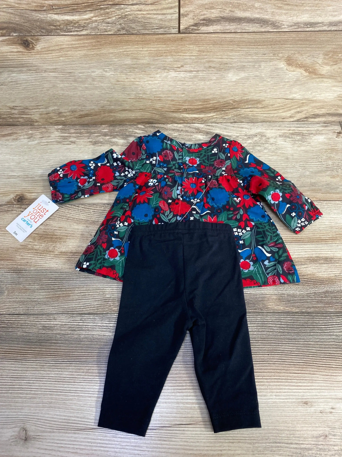Baby girl's long sleeve floral top with red, blue, green flowers and black leggings on wooden floor