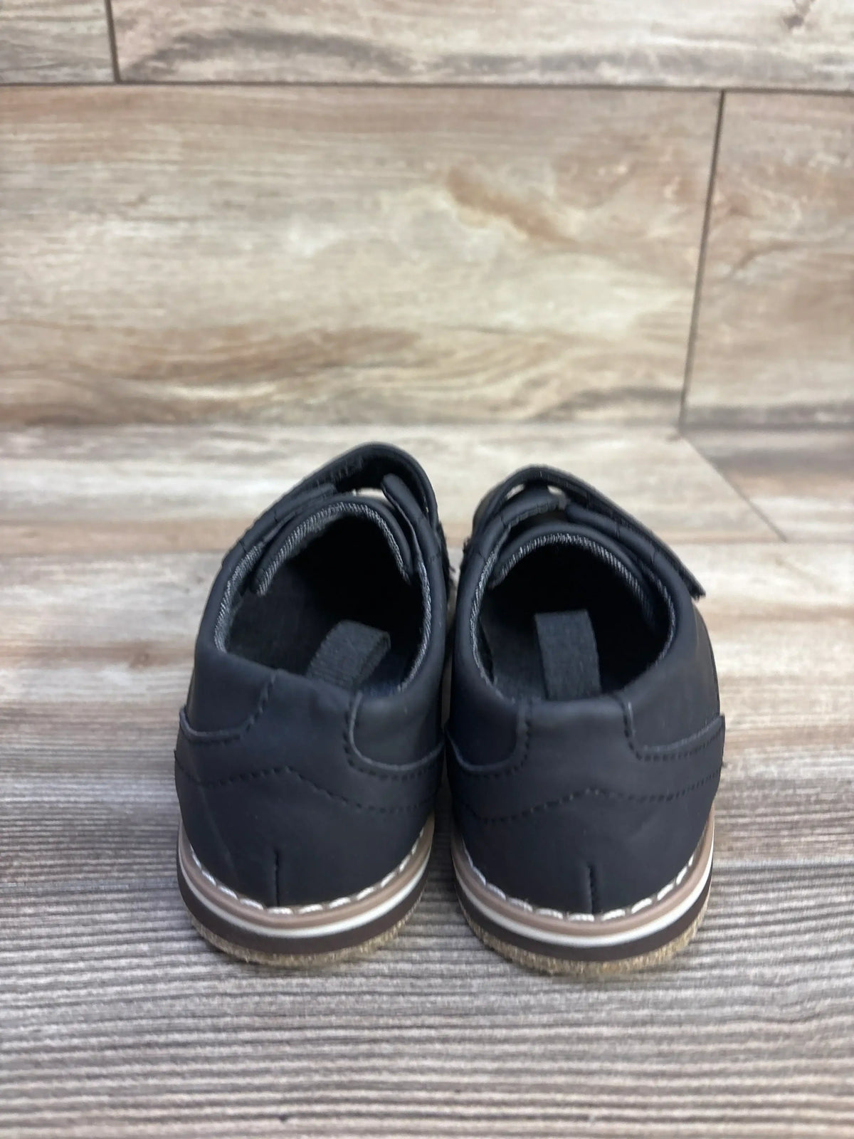 Rear view of Cat & Jack Adonis toddler derby shoes in black showcasing stitched welt and rubber soles on wood-look background